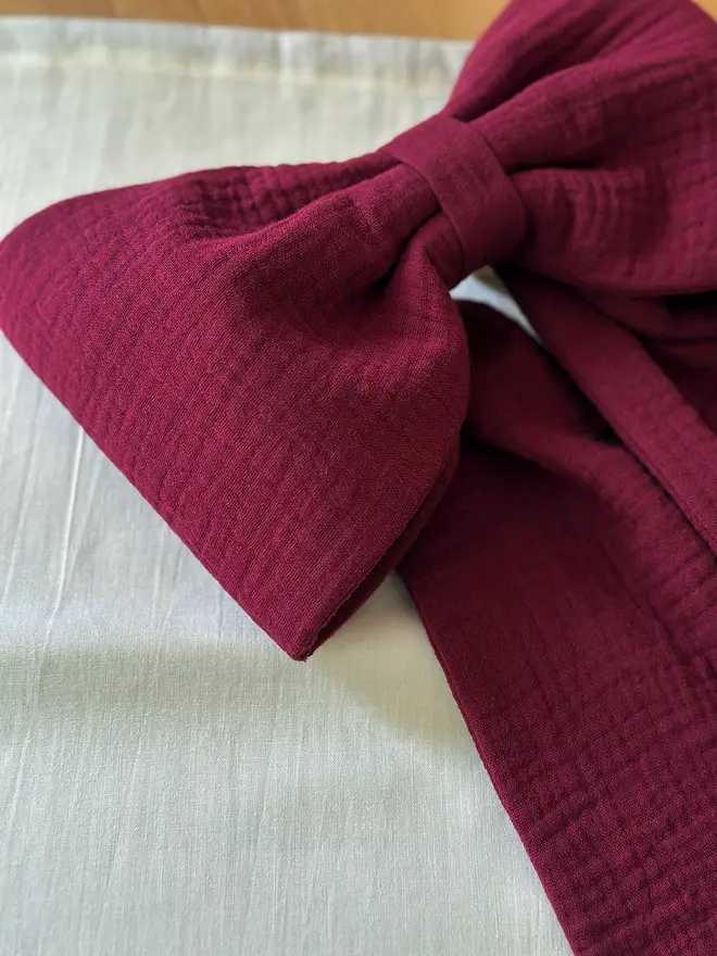 A handmade burgundy Christmas bow made from double gauze cotton fabric.