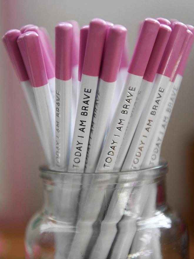 A glass jar full of white pencils with pink tips and the words "Today I Am Brave" along the side of each one.