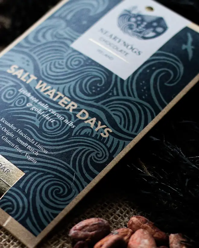 Salt Water Days Chocolate Bar , a chocolate bar sitting on a fabric surface. It is accompanied by some nuts 