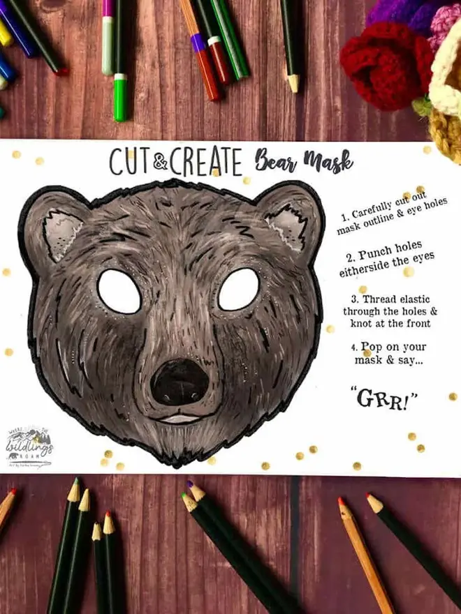 Cut And Create Forest Animals Children’s Masks Kit, an illustrated bear face, surrounded by coloured pencils on a dark wood background.