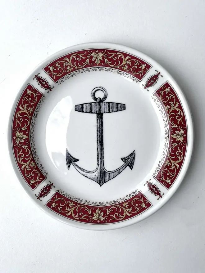 vintage plate with an ornate border, with a printed vintage illustration of an ship's anchor in the middle 