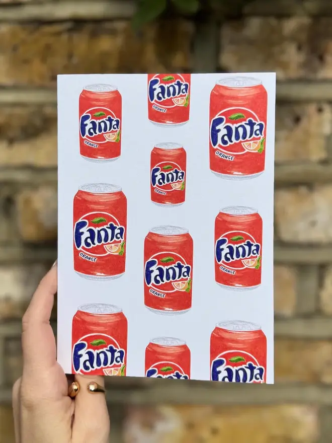 fanta cans illustrated card. card photographed against brick wall background.