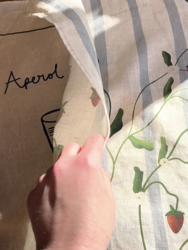 'Strawberry Vines' Linen Tea Towel, a person holding a tea towel with a strawberry motif on it. 