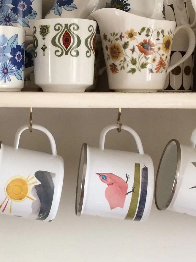 Enamel mugs hang below a shelf full of vintage crockery