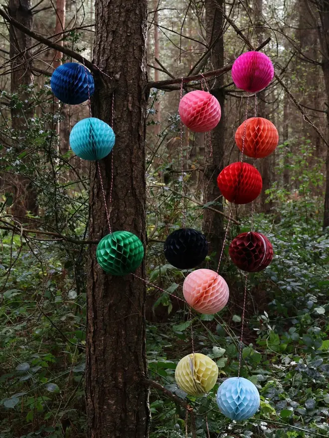 colourful paper ball garland. a string garland with paper balls in assorted colours hanging from trees.
