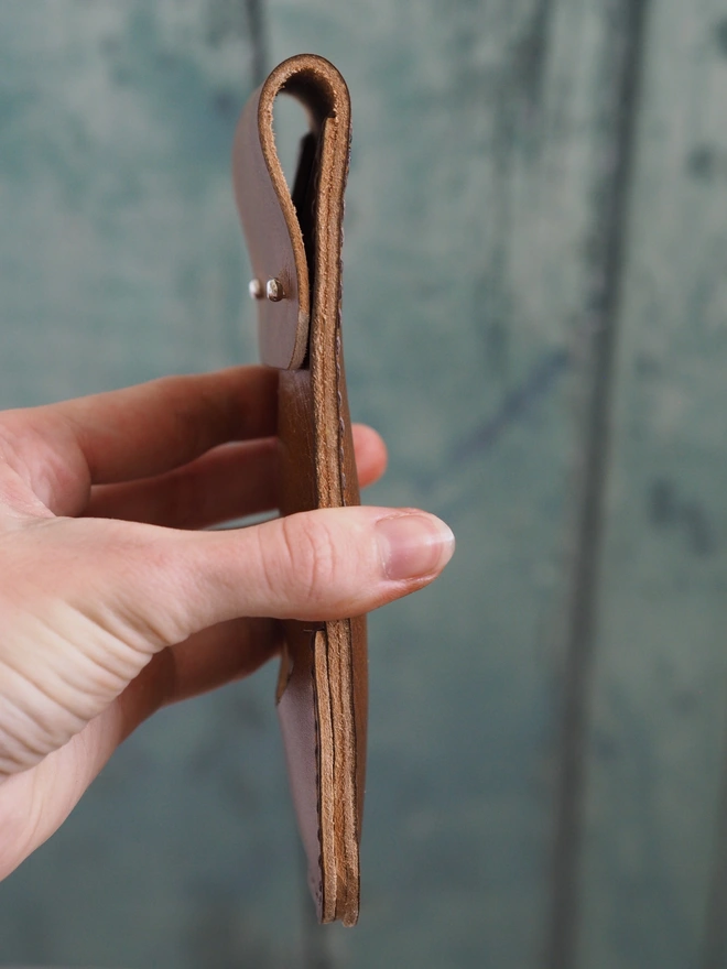A hand hold a small slim leather darts case.