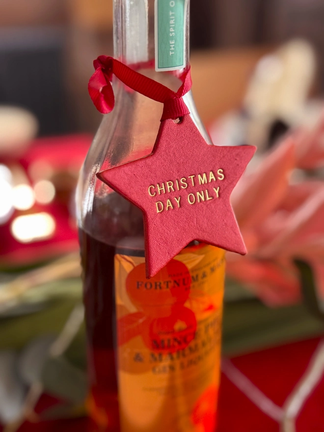 red leather star attached to a bottle of champagne, with gold lettering saying Christmas day only