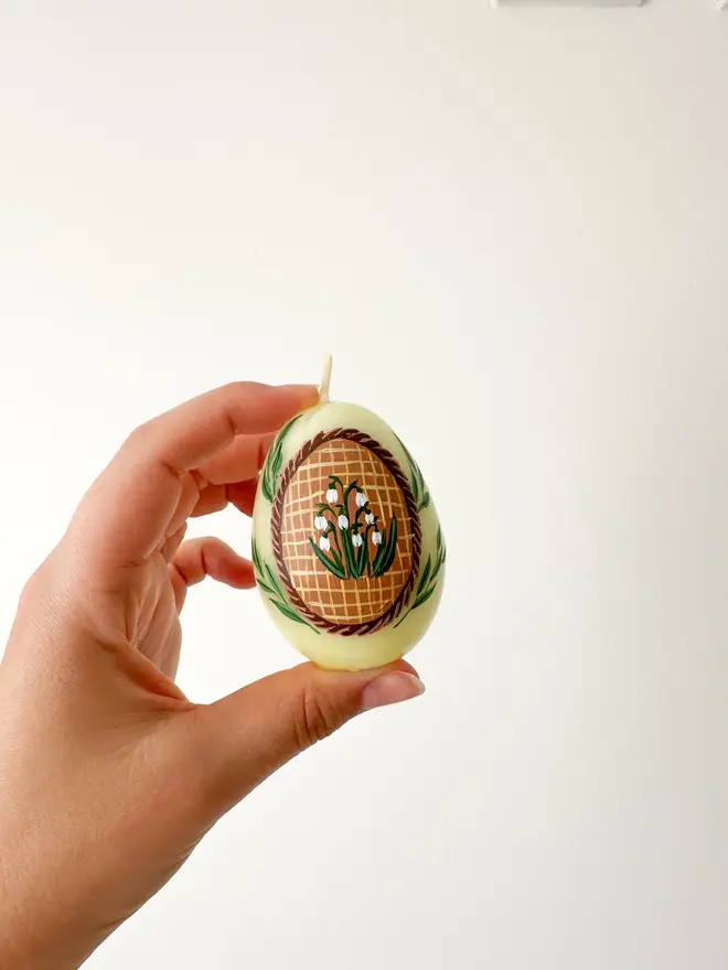 Hand Painted Easter Egg Candle Snowdrops, a woman holding a yellow Easter egg candle against a plain backdrop. 
