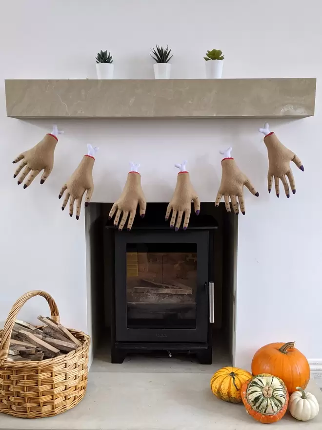 A garland of felt severed hand plushies adorn a fireplace with pumpkins on the hearth