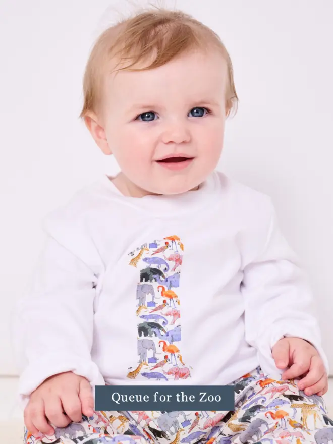 a little boy wearing a white birthday t-shirt with a number 1 cut from liberty queue for the zoo animal print on the front