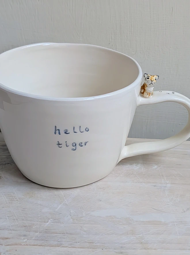 Handmade hello tiger cup in white earthenware ceramic with a tiny stripy cat and hand painted words