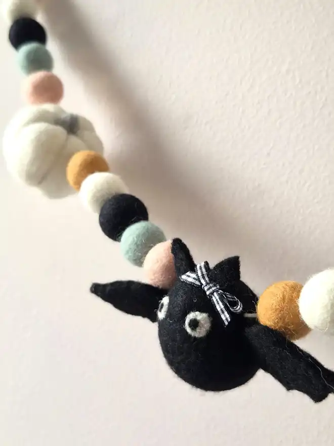 A black felt bat with a black and white gingham bow, hung in a Halloween garland.