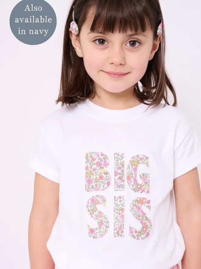 a little girl in a white t-shirt that says Big Sis in the front in floral print