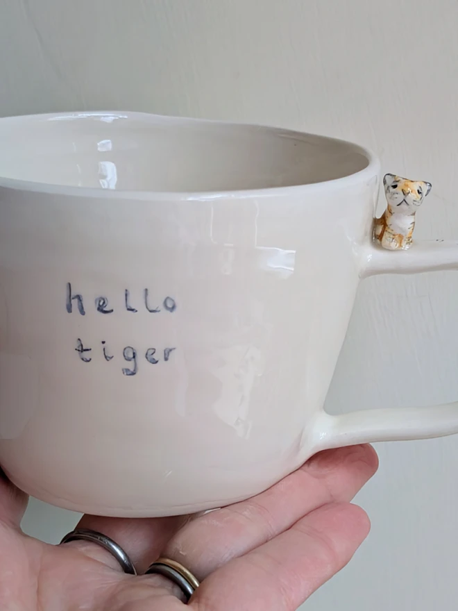 Handmade hello tiger cup in white earthenware ceramic with a tiny stripy cat and hand painted words