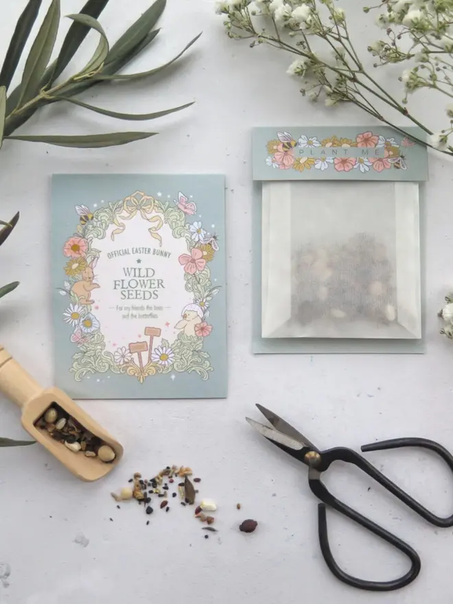 A sage blue "Wild Flower Seeds" card that reads "For my friends the bees and the butterflies." A glassine pouch of mixed seeds, a wooden scoop and black scissors sit alongside.