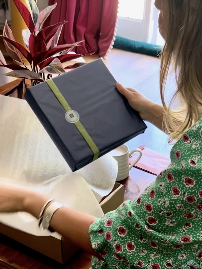 A woman holding a gift wrapped wedding guest book in her hand. 
