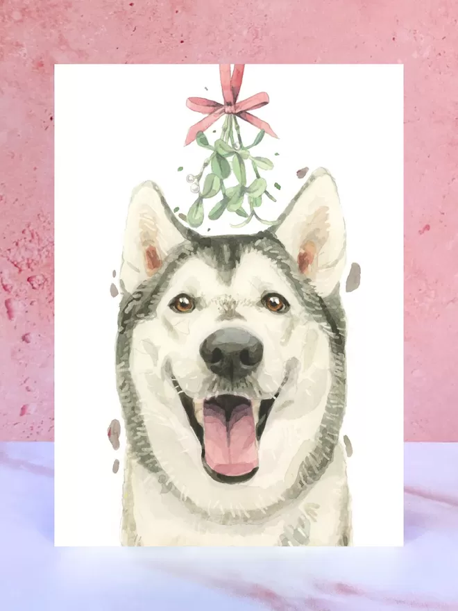 A Christmas card featuring a hand painted design of a Husky, stood upright on a marble surface.