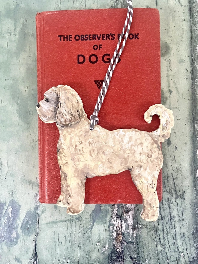 Cream Labradoodle Wooden Hand painted Christmas Decoration placed onto a red book about dogs