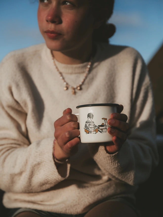 a young girl holding a vintage style enamel illustrated mug
