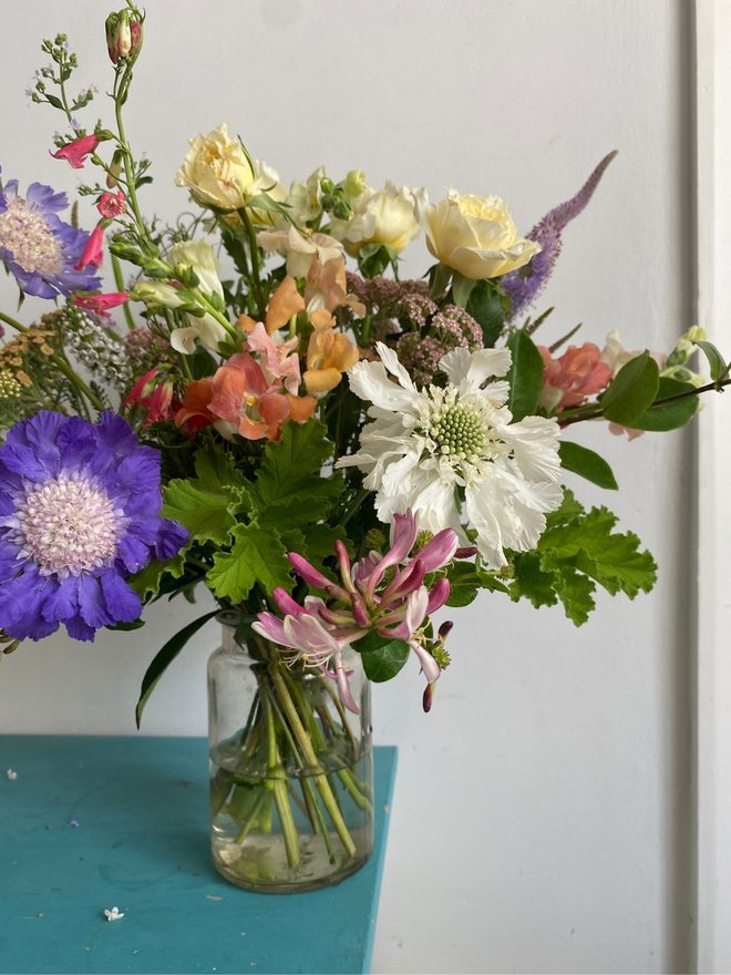 English garden bouquet flower box featuring a wild, hand-tied mix of pastel and bright seasonal blooms, including scented roses, mint, and soft garden foliage, freshly picked in Hampshire for July.