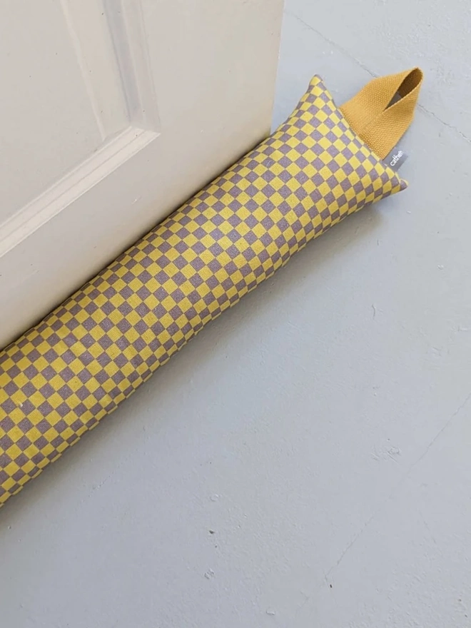 Draught Excluder, a colourful patterned draught excluder sitting on the floor by a white door. 