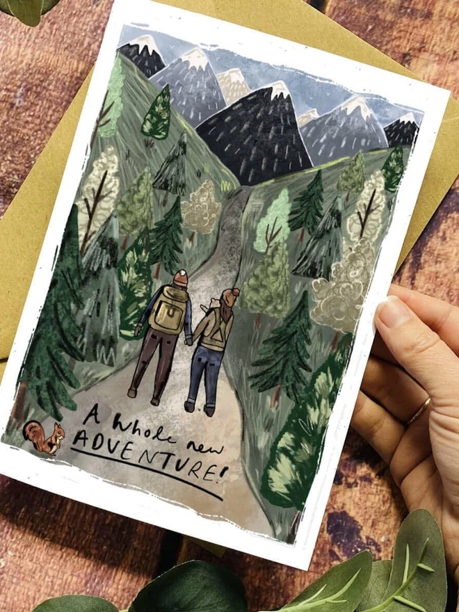 Personalised New Adventure Card, a person holding an adventure themed card above a wooden surface. 