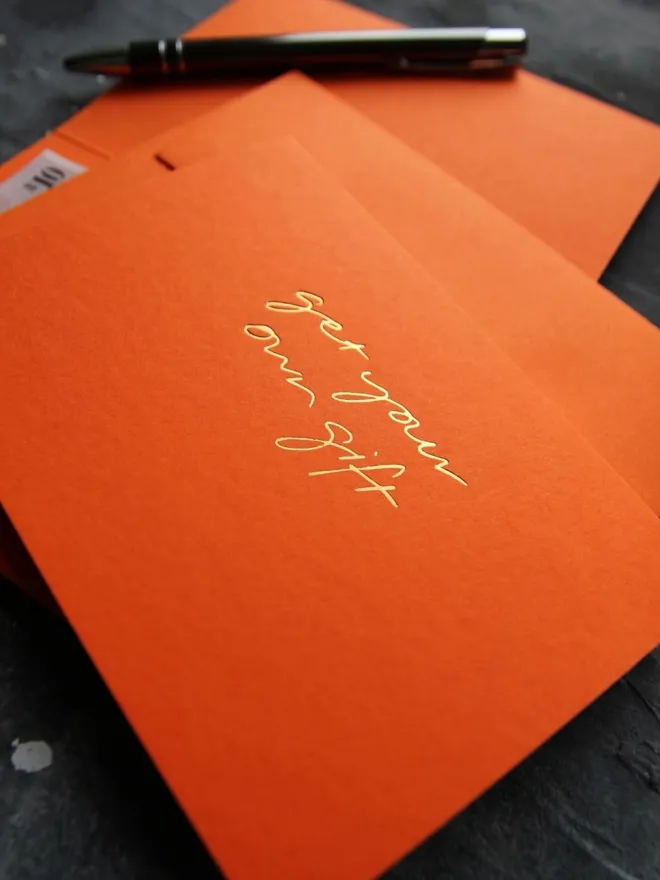 Hand foiled cash card or money wallet in a mandarin colour handfoiled in shiny golf foil text which says ‘get your own gift’.