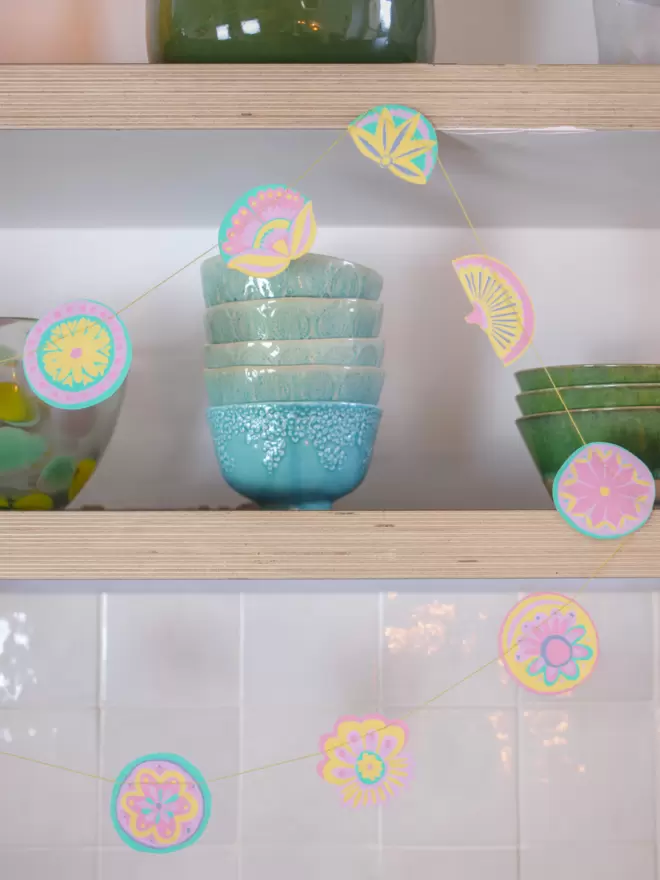 Pastel garland hanging on wooden shelves, accompanies by light blue and green bowls