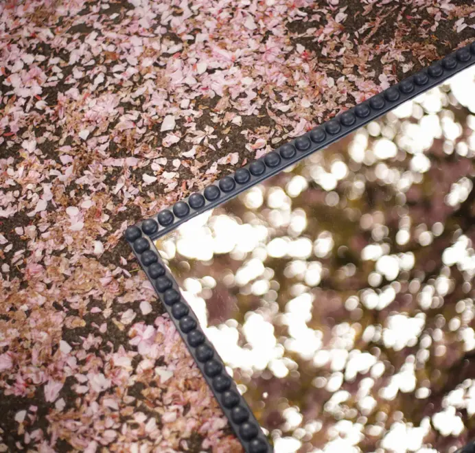 Floor-length bobbin mirror with a turned wooden frame standing among tall grass outdoors.