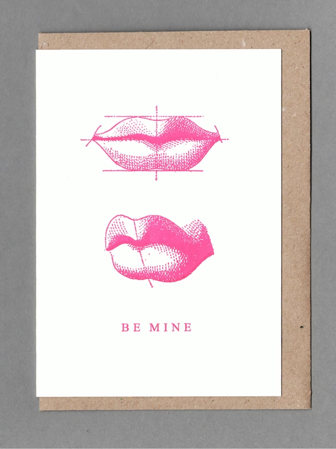 White card with two illustrations of pink lips with text reading 'Be Mine' with a brown envelope behind