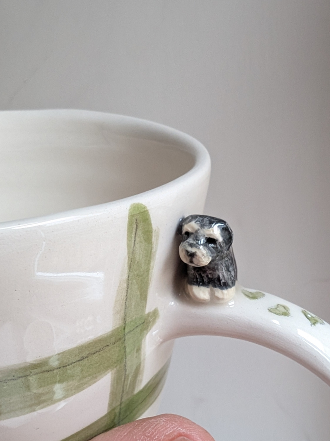 close up of a ceramic green check mug with a miniature cavapoo figure on the handle and hand painted and hearts 