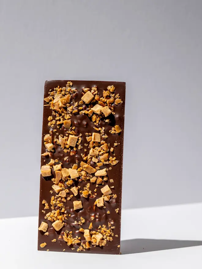 Honeycomb, toffee & fudge chocolate tablette standing on a white table. 