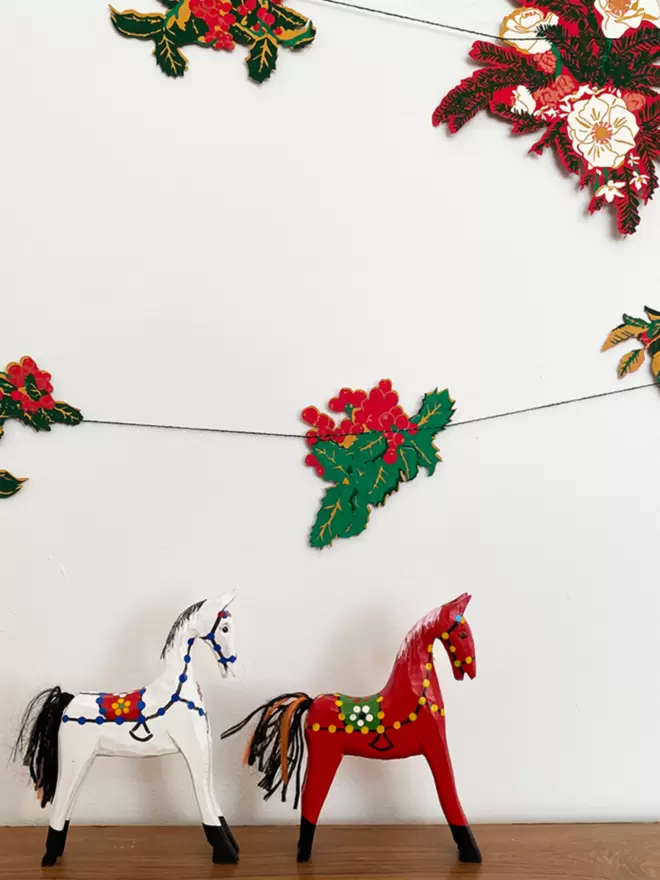 Christmas garland hanging over wall with wooden horses below