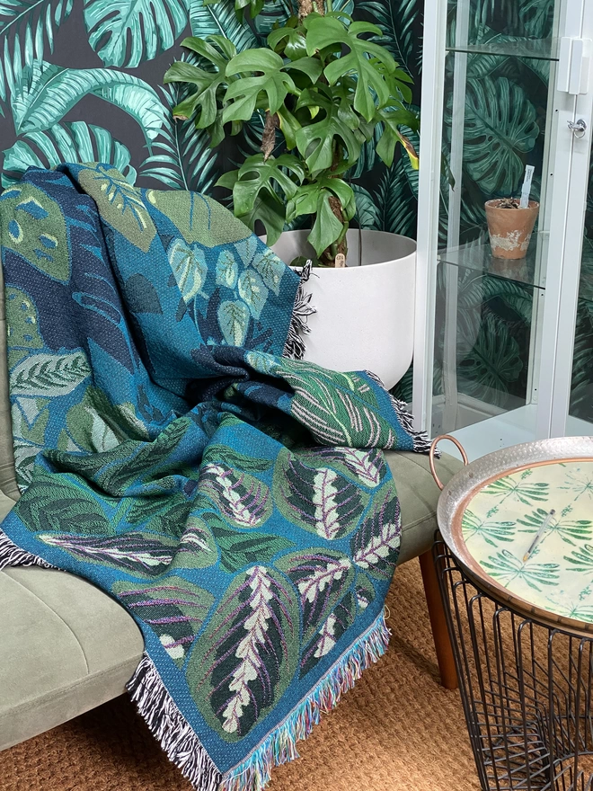 Indoor Jungle Window Blanket seen on a green sofa with plant wallpaper.