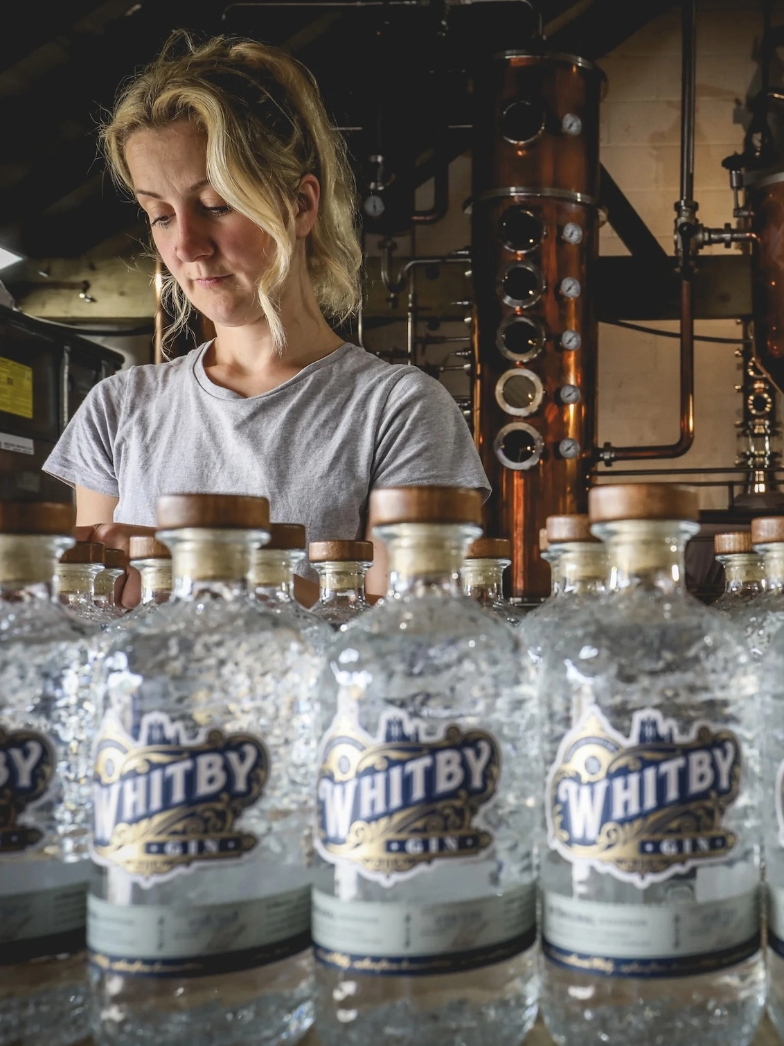 Original Edition Gin, a woman standing with a group of gin bottles on a counter. 