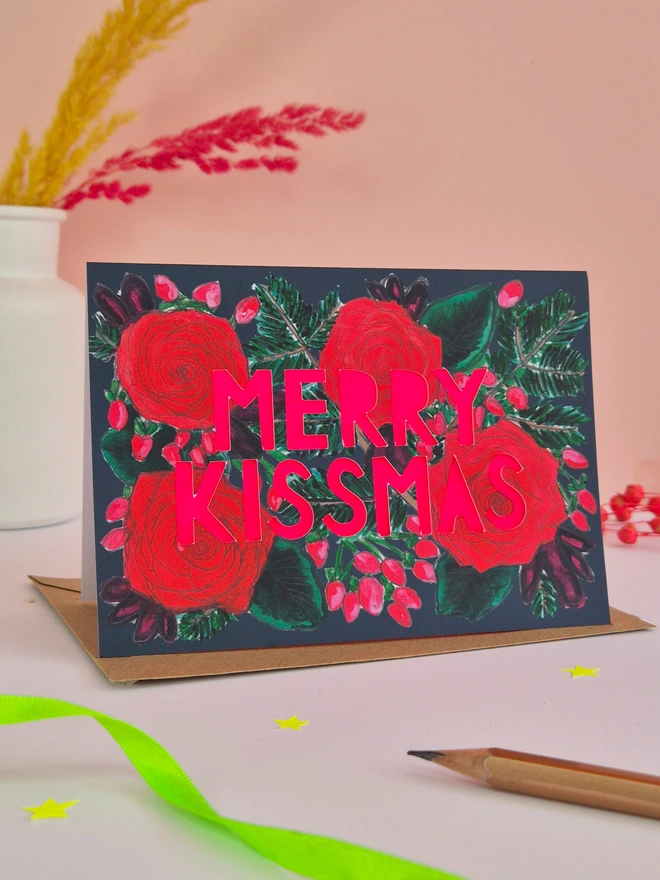 Rose Print Christmas Card with Merry Kissmas in paper cut text and a neon pink paper liner 
