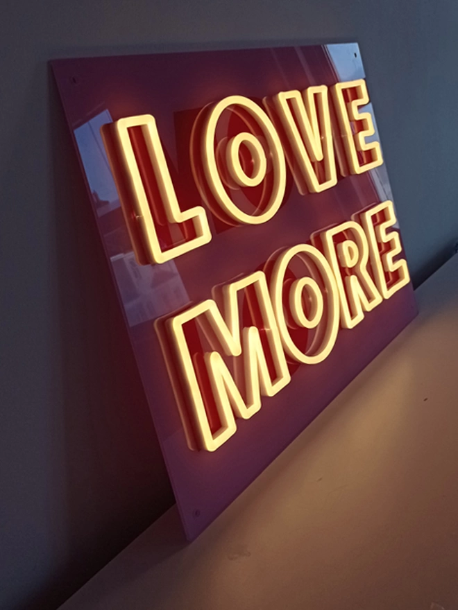'Love More More Love' neon sign switched on