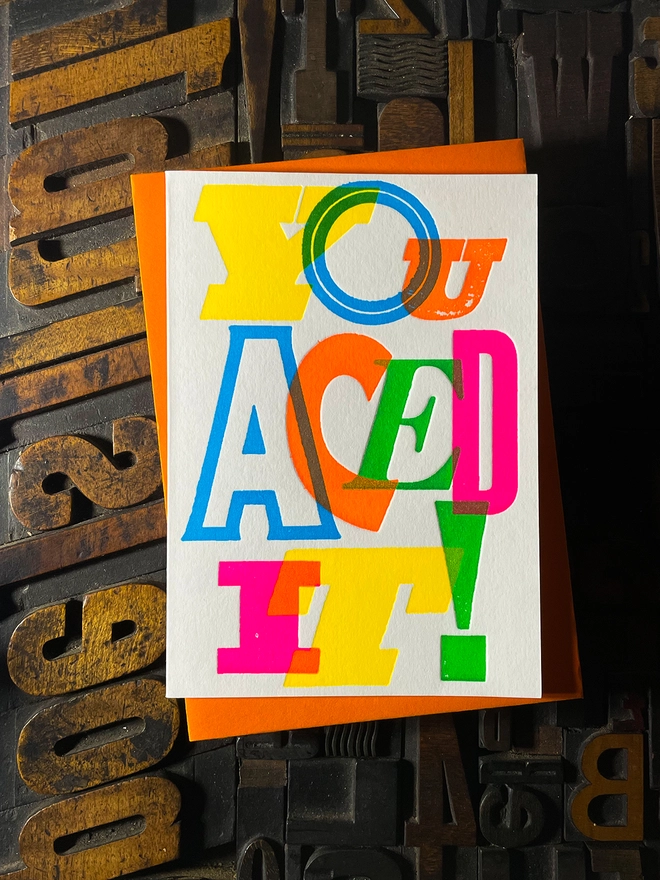 Colourful typographic letterpress card with bold overlapping neon letters spelling ‘You Aced It!’, perfect for celebrating exam success.