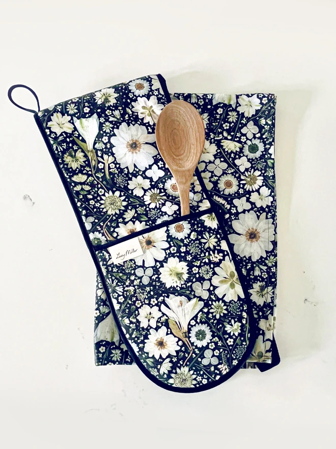 Floral double oven gloves and tea towel with pressed white flower design on a black background. Complete with hanging loop.