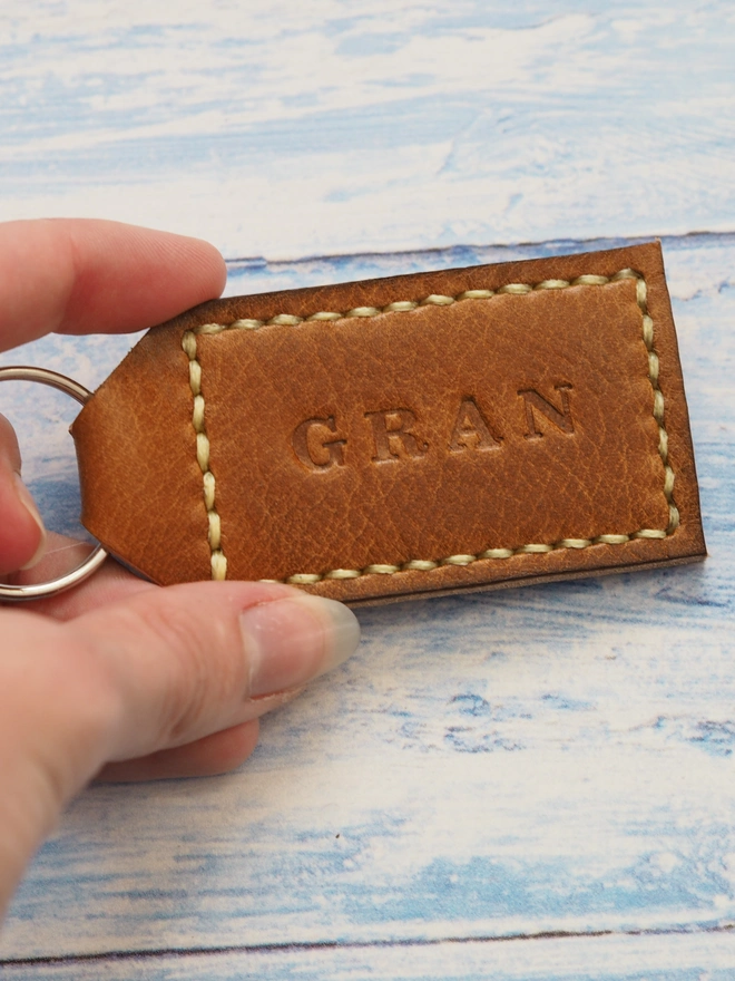 Personalised tan brown leather key ring. Handmade tan brown tag shaped keyring stitched with pale yellow thread. Stamped with the name GRAN.