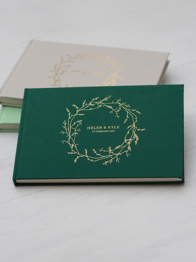 Personalised Wedding Guestbook. A personalised hardcover wedding guestbook with a delicate gold vine wreath illustration on the front and personalise with names and a date. 