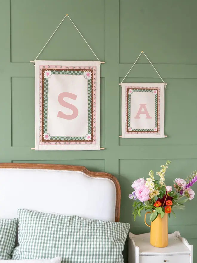 Personalised Cottagecore Initial Fabric Banner, hanging against a green wall. 
