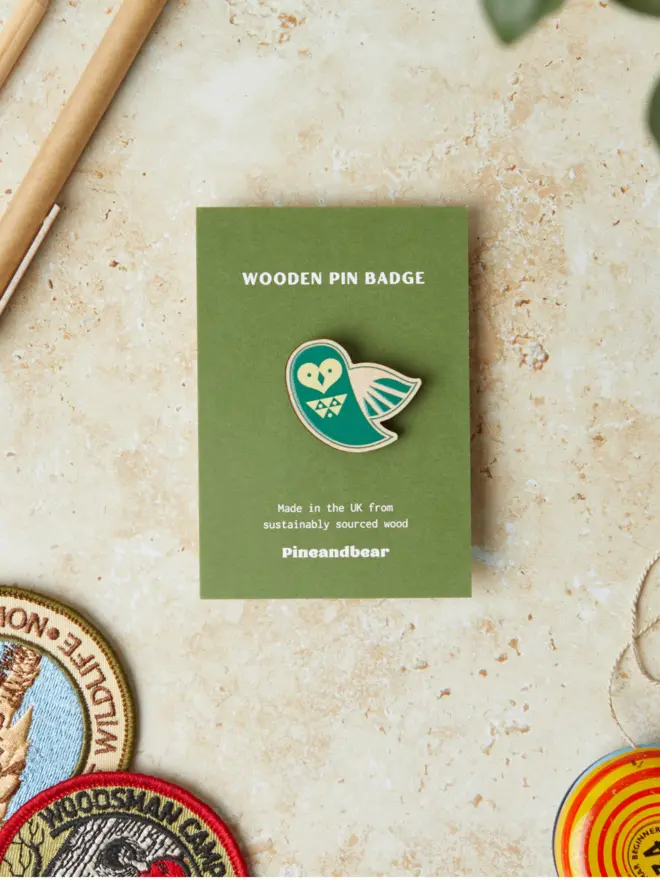 Wooden owl pin badge on a green presntation card