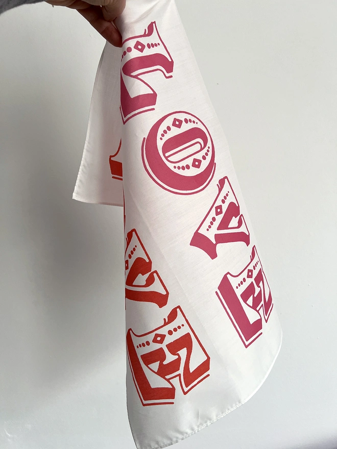 A white hand holds a Mr.PS Love Love Love Handkerchief against a white wall