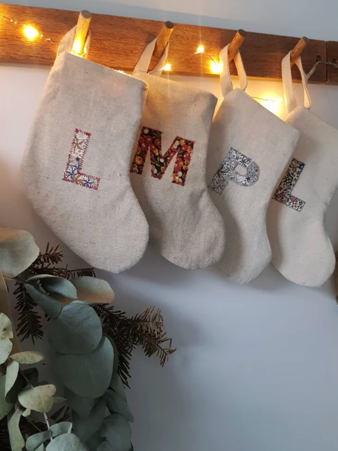 Mini Christmas Stocking with Floral Fabric Initial. Several stockings with a variety of linen letters hanging on a wall.
