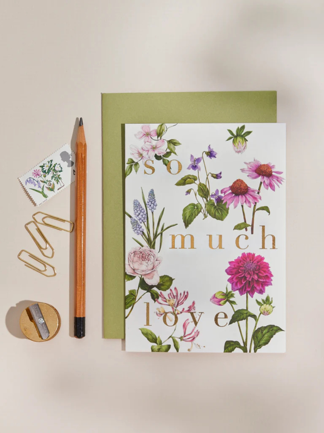 'so much love' illustrated floral card. a white floral card and green envelope photographed against a plain background. 
