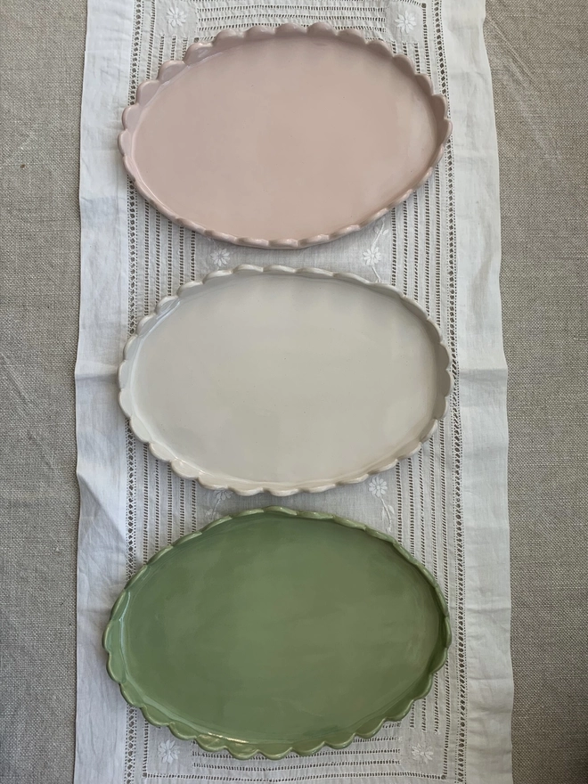 three oval cake plates with stand up scalloped edges, pale pink, sage green and white, top view