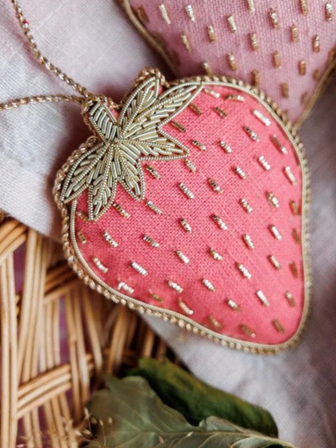 strawberry embroidered linen decoration. pink beaded strawberry ornament presented in wicker basket.