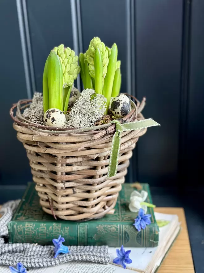 Rattan basket filled with hyacinths sitting on top a stack of books finished with quail eggs and moss