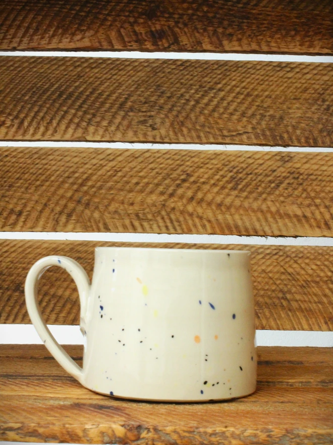 Large creamy white terrazzo cups with black, blue, and yellow splatters and glossy glaze on a wooden table